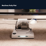 A Riccar under-desk mat shown on a carpeted floor under a table, with a dark overlay at the top reading 'Reclines Fully Flat'.